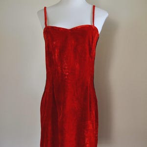 May include: A bright red velvet dress with delicate spaghetti straps. The dress features a sweetheart neckline and a fitted shape, presented on a white mannequin. The dress is a mini length.