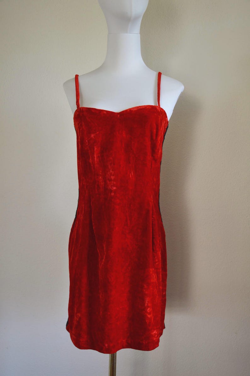 May include: A bright red velvet dress with delicate spaghetti straps. The dress features a sweetheart neckline and a fitted shape, presented on a white mannequin. The dress is a mini length.
