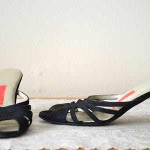 Könnte beinhalten: Ein Paar schwarze Wildledersandalen mit Absatz und einem Kreuzriemen-Design. Die Sandalen haben einen niedrigen Absatz und eine offene Zehenpartie.