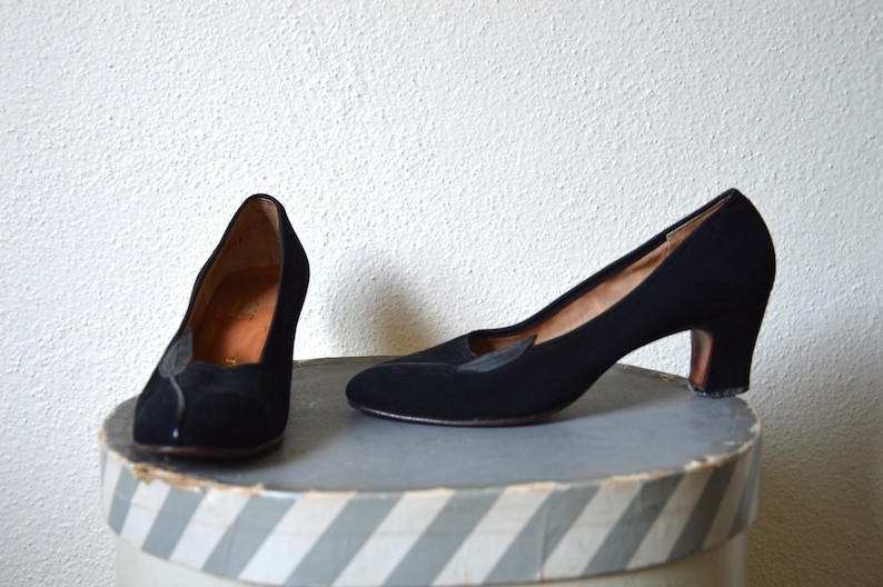 May include: A pair of black suede heeled pumps with a pointed toe. The shoes have a small decorative detail on the vamp.