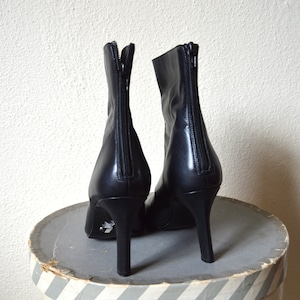 May include: A pair of black leather ankle boots with a pointed toe and a high heel. The boots have a zipper on the back and a decorative detail on the heel.