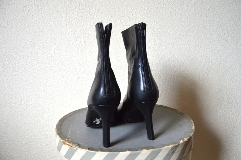 May include: A pair of black leather ankle boots with a pointed toe and a high heel. The boots have a zipper on the back and a decorative detail on the heel.