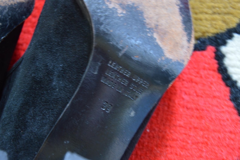 May include: Close-up of the sole of a black shoe. The sole is marked with the words "LEATHER UPPER, LEATHER SOLE, MADE IN ITALY" and the number "39". The shoe's sole shows signs of wear.