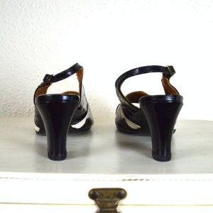 May include: A pair of black heeled shoes with white trim. The shoes have a slingback design and a pointed toe.