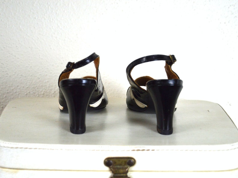 May include: A pair of black heeled shoes with white trim. The shoes have a slingback design and a pointed toe.