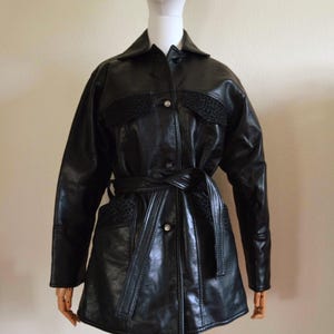May include: A black leather jacket with a collared neckline, long sleeves, and a belted waist. The jacket has decorative panels and button fastenings. The jacket is displayed on a mannequin.