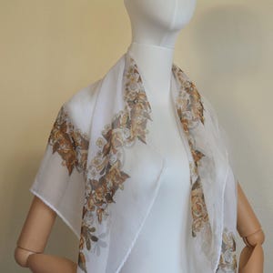 Può includere: Un foulard bianco di chiffon con un motivo floreale marrone. Il foulard è su un manichino bianco.