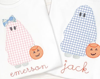 May include: Two white t-shirts featuring embroidered ghost designs. The left ghost is pink gingham with a blue floral bow, and the right ghost is blue gingham. Both hold orange jack-o'-lantern buckets. The names emerson and jack are stitched below.