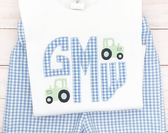 Puede incluir: Una camisa blanca de manga corta con un estampado de cuadros azules y blancos, monogramada con la letra "G" y dos tractores de juguete verdes. La camisa se combina con pantalones cortos de cuadros azules y blancos.