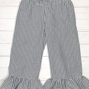 May include: A pair of pants featuring a black and white gingham check pattern. The pants have an elasticized waistband and wide legs that finish with a gathered ruffle detail at the bottom hem, creating a distinct flared silhouette throughout.
