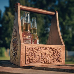 May include: Wooden beer caddy with a handle, holding three bottles of beer. The caddy is intricately carved with a detailed relief design. The wood has a warm, natural tone, and the bottles are filled with a golden liquid.