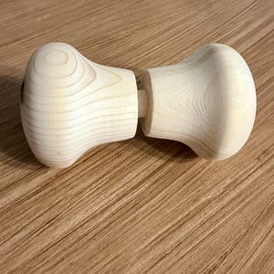 May include: Two-piece wooden dumbbell with a light, natural wood grain finish. Each end is rounded, connected by a short, cylindrical peg. The dumbbell is designed for exercise and fitness.