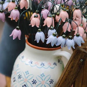 Può includere: Un'anfora di ceramica bianca con un motivo floreale blu e rosa, riempita di un bouquet di fiori di ceramica rosa e viola.