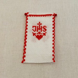 May include: White fabric with red embroidered border and a red embroidered monogram of "JHS" with a cross above the letters.
