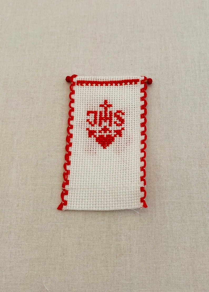 May include: White fabric with red embroidered border and a red embroidered monogram of "JHS" with a cross above the letters.
