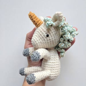 May include: A white crocheted unicorn toy with a light blue and gold mane, a brown horn, and gray hooves.