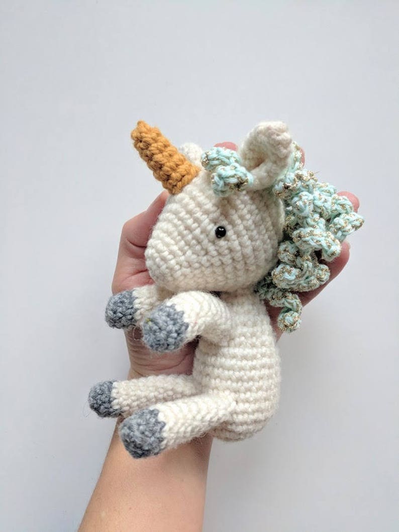 May include: A white crocheted unicorn toy with a light blue and gold mane, a brown horn, and gray hooves.