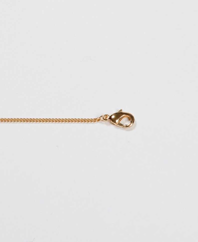 May include: A gold-colored necklace chain with a lobster clasp. The chain is a delicate curb style, and the clasp is a rounded shape. The necklace is shown against a white background.