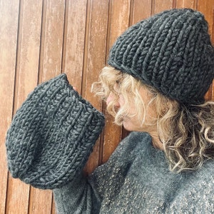 Può includere: Un berretto di lana grigio e un cappello slouchy abbinato. Il berretto è ripiegato verso il basso e il cappello slouchy è indossato sulla testa di una persona con i capelli lunghi e ricci.