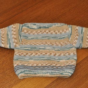 Peut inclure: Un pull en tricot rayé dans les tons de bleu, marron et blanc. Le pull a un col rond et des manches longues.