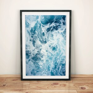 Puede incluir: Una fotografía enmarcada de un primer plano de olas del océano que rompen y crean espuma blanca. El agua es de un color azul profundo.