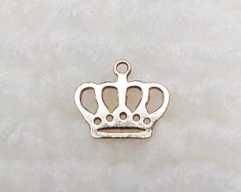 May include: A gold-colored crown charm with a loop at the top for hanging. The crown has a classic design with five arches and small circular details along the base. The charm is set against a white, textured background.