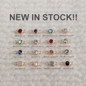 May include: A selection of gold-plated connectors, each with a different coloured gemstone. Gemstones include garnet, amethyst, aquamarine, and clear crystal. The text "NEW IN STOCK!!" is displayed at the top of the image.