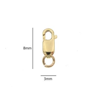 May include: A gold-colored lobster clasp, 8mm in length and 3mm wide, with a spring-loaded mechanism. The clasp has a rounded shape with a small ring at the bottom for attaching jewelry. The background is white.