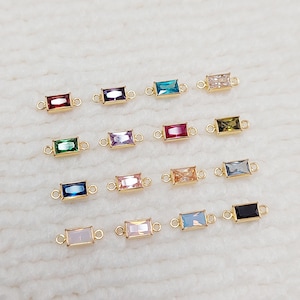 以下が含まれることがあります： 赤、緑、青、ピンクなど、さまざまな色の長方形の宝石コネクタのコレクションで、金色の金属にセットされています。各コネクタには、他のジュエリーコンポーネントに取り付けるための2つの小さなループがあります。宝石は長方形にカットされています。