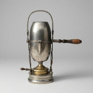 May include: A vintage metal coffee percolator featuring a cylindrical silver-toned body, a brass-colored base, and a vertical arched handle. It includes a horizontal wooden handle on the side and a small wooden lever near the base for operation.