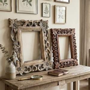 Op de afbeelding: Twee rechthoekige houten fotolijsten met ingewikkelde, met de hand gesneden bloem- en krulpatronen. De grotere lijst heeft een lichte, verweerde afwerking, terwijl de kleinere lijst een donkerdere, gepolijste houttint heeft met golvende details.
