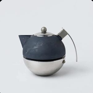May include: A spherical teapot featuring a matte dark gray upper body and a polished silver metallic lower base. It includes a matching dark gray lid with a small silver knob, a short spout, and a curved silver handle extending from the side.