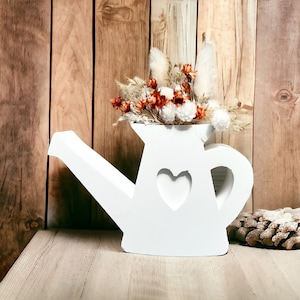 Puede incluir: Riego de madera blanco con un recorte en forma de corazón, lleno de flores secas en tonos de blanco y naranja. El riego está sentado sobre una superficie de madera.