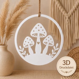 May include: A white circular hanging ornament featuring a cutout design of three mushrooms with spotted caps and a small heart on the central stem, suspended by a brown twine cord. A circular badge in the corner displays the text 3D Druckdatei.