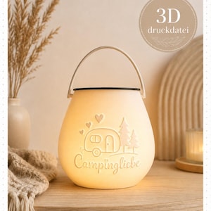 Könnte beinhalten: Eine cremefarbene, leuchtende Laterne mit Henkel, die ein geprägtes Design eines Wohnwagens, Tannenbäumen und kleinen Herzen zeigt. Der Schriftzug 'Campingliebe' ist vorne eingeprägt. Ein kreisförmiges Abzeichen in der Ecke zeigt '3D druckdatei'.