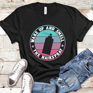 May include: Black t-shirt with a retro-style graphic of a hairspray can and the text "Wake Up And Smell The Hairspray".