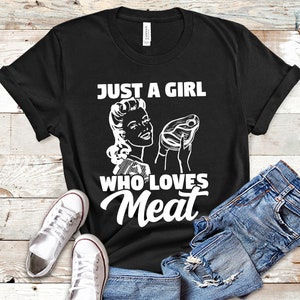 May include: Black t-shirt with a white graphic of a woman holding a steak and the text "Just a girl who loves meat".