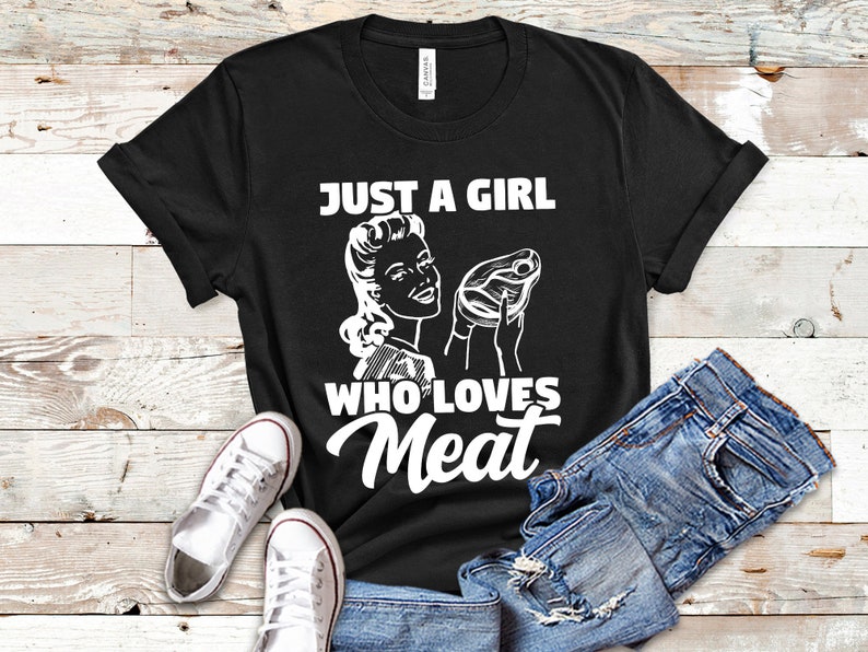May include: Black t-shirt with a white graphic of a woman holding a steak and the text "Just a girl who loves meat".