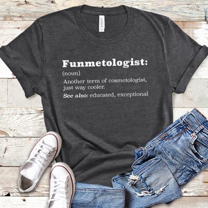 Può includere: Una maglietta grigio scuro con testo bianco che recita "Funmetologist: (nome) Un altro termine per cosmetologo, semplicemente più cool. Vedi anche: istruito, eccezionale"