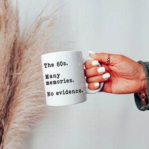 May include: White ceramic mug with black text that reads "The 80s. Many memories. No evidence."