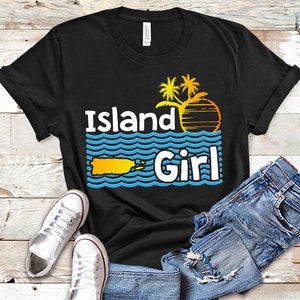 May include: Black t-shirt with a graphic design of a palm tree silhouette, a sunset, and the text "Island Girl" with a blue outline. The graphic also includes a yellow outline of the island of Puerto Rico.