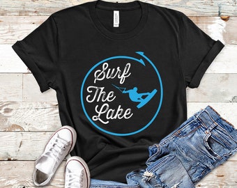 May include: Black t-shirt with a blue circle graphic that says "Surf The Lake" in white text. A silhouette of a person wakeboarding is inside the circle.