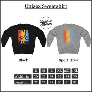 May include: Unisex sweatshirt with a black and grey color option. The sweatshirt features a retro-style graphic of a BMX bike with the text "BMX MOM" in colorful letters. The size chart shows the width and length in inches for sizes S through 3XL.