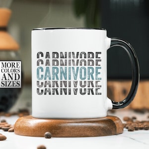 May include: White ceramic mug with a black handle. The mug has a distressed graphic design that says "CARNIVORE" in a blue and gray color scheme.