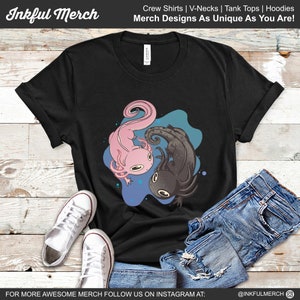 K&ouml;nnte beinhalten: Schwarzes T-Shirt mit einem rosa und schwarzen Axolotl-Design. Die Axolotl sind vor einem blau-t&uuml;rkisfarbenen Hintergrund platziert. Das Shirt tr&auml;gt auch den Text "Inkful Merch" und "Merch Designs As Unique As You Are!"