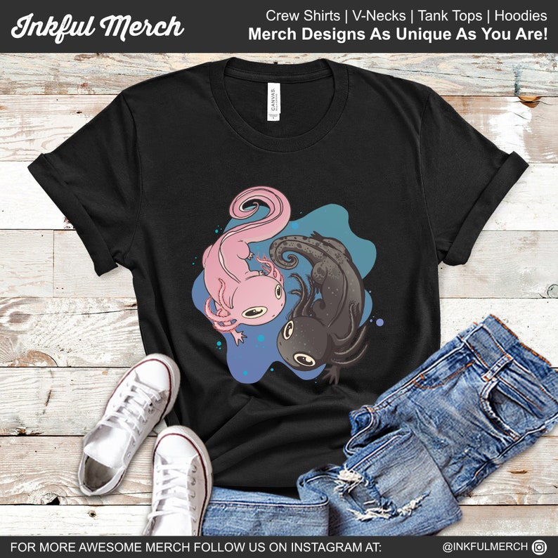 K&ouml;nnte beinhalten: Schwarzes T-Shirt mit einem rosa und schwarzen Axolotl-Design. Die Axolotl sind vor einem blau-t&uuml;rkisfarbenen Hintergrund platziert. Das Shirt tr&auml;gt auch den Text "Inkful Merch" und "Merch Designs As Unique As You Are!"