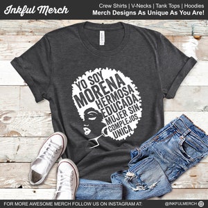 May include: A dark gray t-shirt with a white graphic design of a woman's face with an afro hairstyle. The text on the graphic reads "Yo soy Morena Hermosa Educada Mujer sin Complejos Unica".