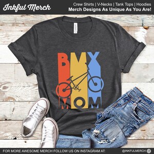 May include: A dark gray t-shirt with a retro-style design featuring a BMX bike and the text "BMX MOM". The design is in shades of red, orange, yellow, and blue.