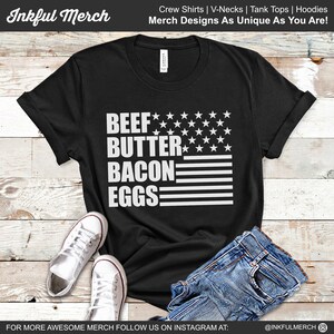 May include: Black t-shirt with a white design of an American flag with the words "BEEF BUTTER BACON EGGS" written vertically.