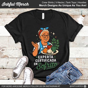 May include: Black t-shirt featuring a cartoon of a woman holding a plate of vegetables, with text that reads "EXPERTA CERTIFICADA EN Sofrito." The shirt is paired with jeans and white sneakers. The top of the image has the text "Inkful Merch" and "Merch Designs As Unique As You Are!"